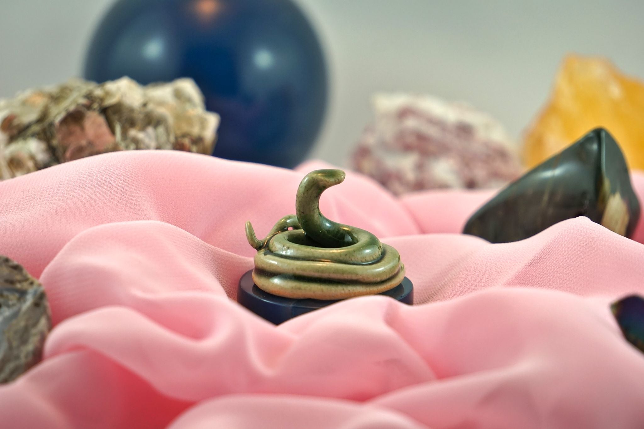 Small, handmade and painted cermaic snake on a bed of pink fabric and crytals. 