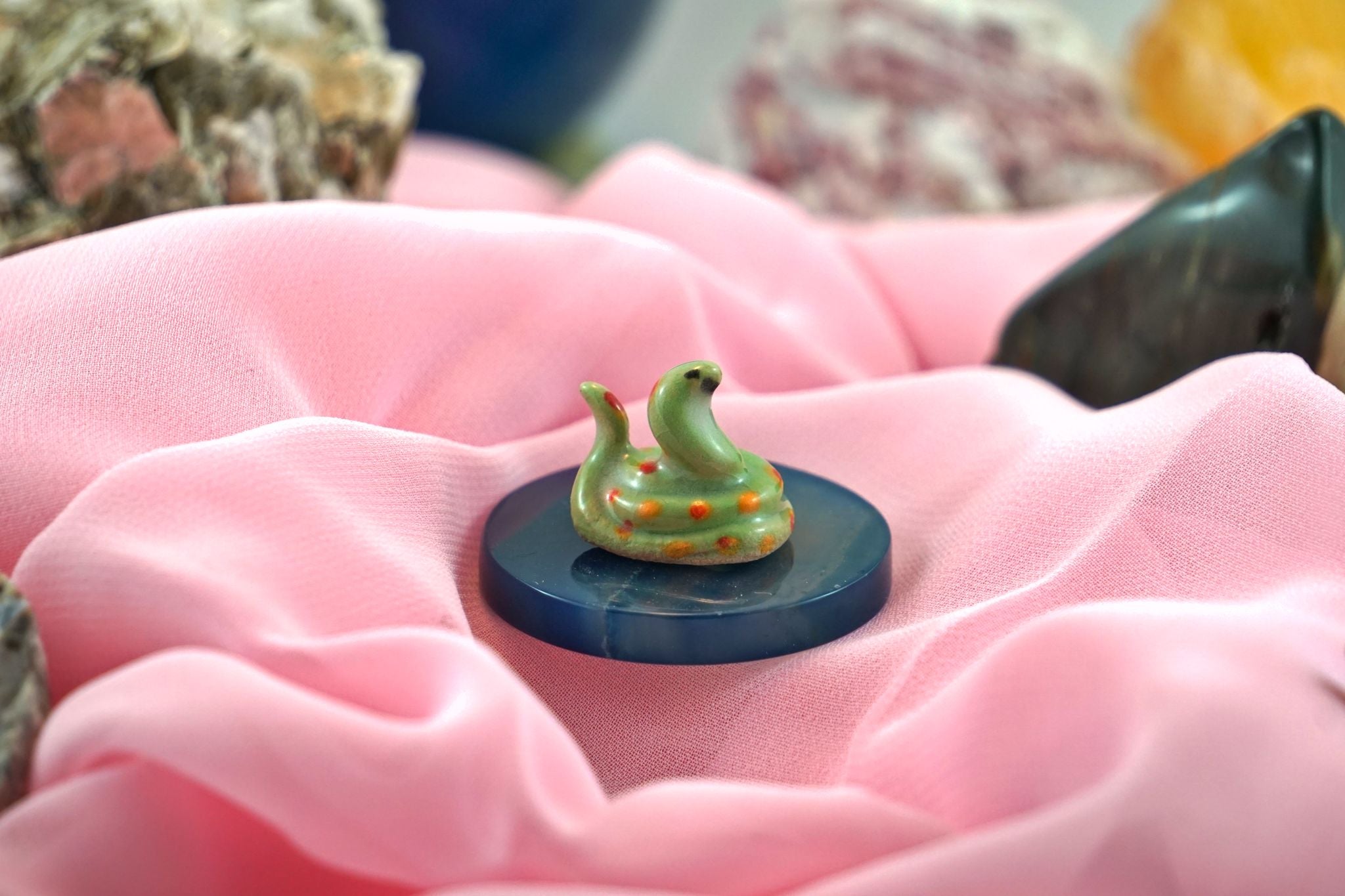 Small, handmade and painted cermaic snake on a bed of pink fabric and crytals. 