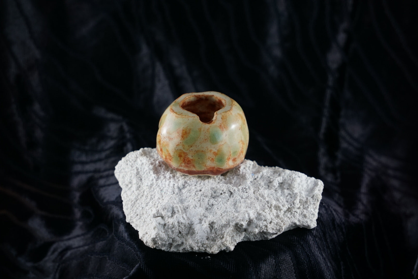 Small, handmade, orange/brown and green ceramic ashtray molded around a piece of white rock.