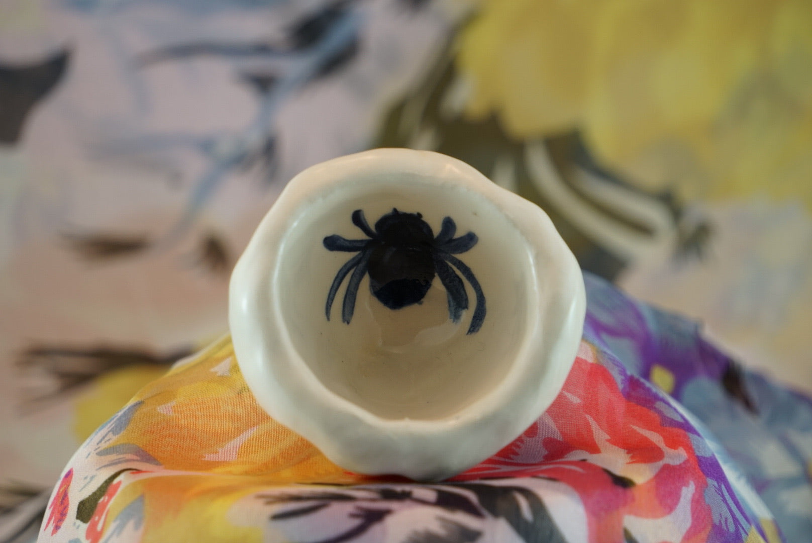 Small, handmade white ceramic pinch pot with loosely drawn blue insects. 